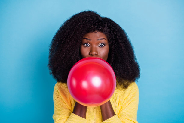 年轻女孩在蓝色背景前吹着粉色气球，准备庆祝节日的特写照片图片下载
