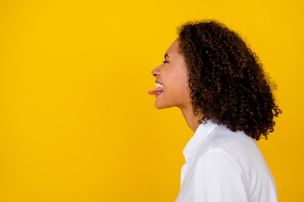 甜美女孩的侧面照片，享受生日派对，庆祝时吐出舌头，闭着眼睛，背景为黄色，空白空间。图片下载