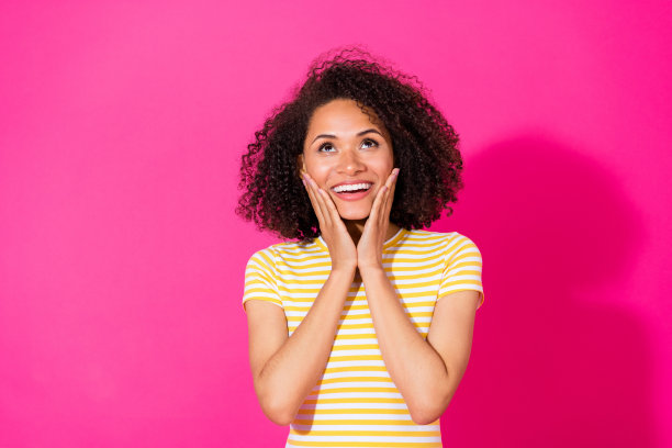 漂亮年轻女孩的照片肖像，手掌托着脸颊，仰望着，穿着时尚的黄色条纹衣服，背景为鲜艳的粉色。图片下载