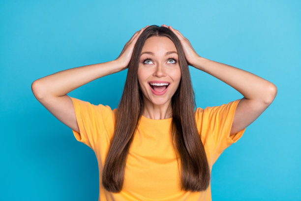特写照片：年轻迷人的女性双手托着头，惊喜地看向上方，背景为蓝色。图片下载