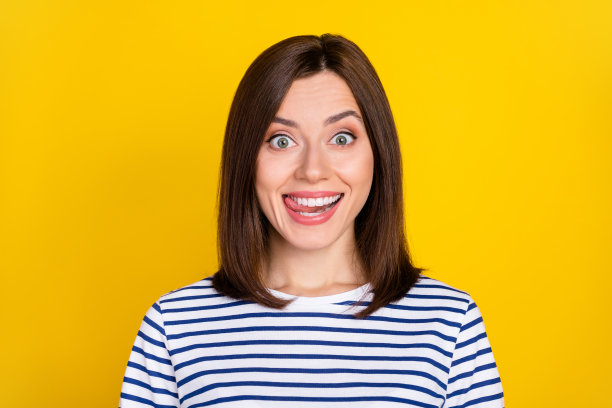 年轻漂亮女士的照片肖像，舌头舔牙齿，饥饿微笑，穿着时尚的条纹衣服，背景为黄色。图片下载