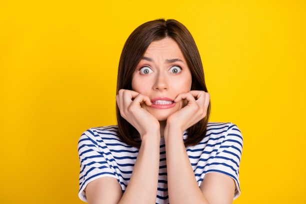 漂亮年轻女性的照片肖像，因坏消息而感到害怕，咬着指甲，穿着时尚的条纹衣服，背景为黄色。图片下载