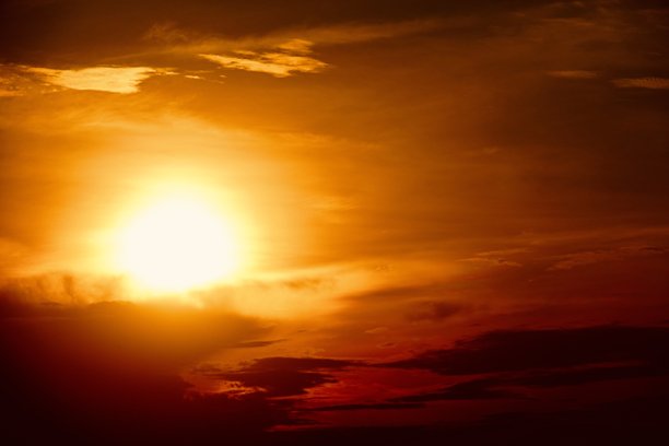 这是一张美丽的日落或日出照片，天空的主要颜色是明亮的橙色、黄色和红色。太阳部分被云层遮挡，使得天空看起来更加明亮和温暖。图片下载