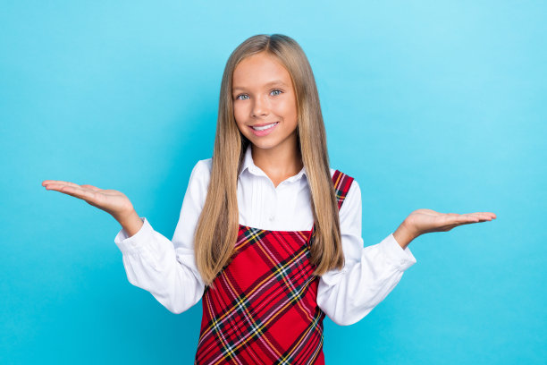 穿着校服的年轻漂亮女孩的肖像照片，双手托着脸颊，露出灿烂的微笑，背景为蓝色。图片下载