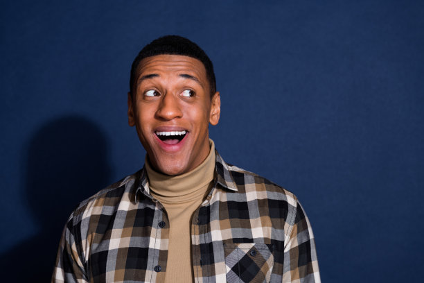 年轻男子的照片肖像，兴奋地望向空旷的空间，穿着时尚的格子服装，背景为深蓝色。图片下载