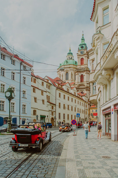 圣尼古拉教堂（小城区）有一个绿色的屋顶（圆顶），位于捷克共和国布拉格市中心。这张图片展示了铺有鹅卵石的街道，路上有复古汽车和电车轨道。图片下载