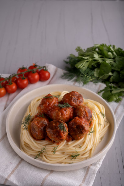 自制意大利面美食照片，盘子里的肉丸和番茄酱，精致的晚餐，餐桌上摆放着新鲜的香草和樱桃装饰。图片下载