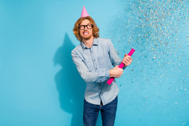 穿着牛仔衬衫、戴着眼镜和帽子的甜美惊讶男士在蓝色背景下拍摄闪光效果的照片图片下载