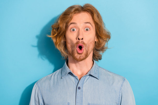 穿着牛仔衬衫、眼睛大睁、嘴巴张开的惊讶时尚男士照片，背景为蓝色。图片下载