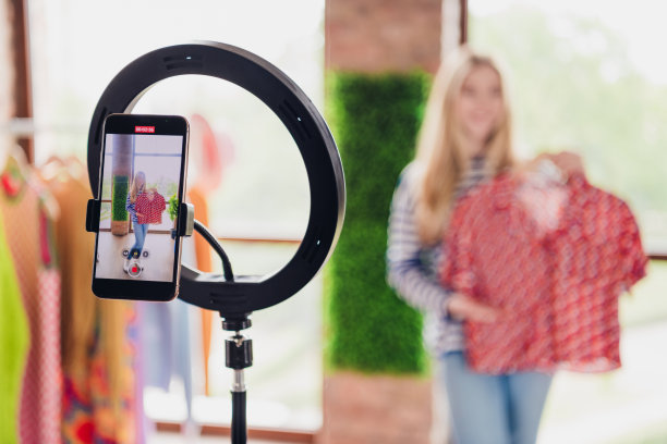 漂亮女孩博主在室内日光下进行社交媒体直播，在线销售服装的照片图片下载