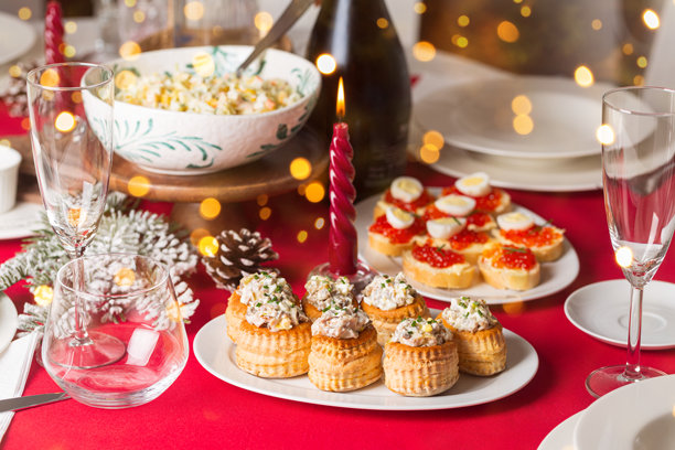 用自制食物、各种开胃菜、鸡肉沙拉的泡芙、鱼子酱和鸡蛋的迷你点心、酒瓶、蜡烛和装饰品布置的圣诞餐桌。红色桌布。生活方式照片，展示晚宴派对、庆祝活动和节日盛会。图片下载