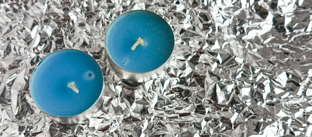 香薰蜡烛放在烛台上，背景为闪亮的银色。蓝色蜡烛放在金属杯中。留有文字空间。这是一张不寻常的照片。图片下载