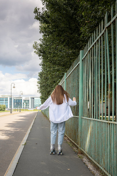 长发美女在公园里滑旱冰。四轮滑冰是一种受欢迎且安全的休闲活动。竖版照片图片下载