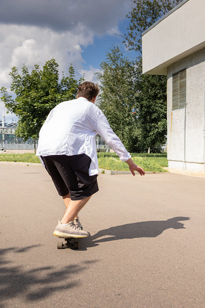 年轻男子穿着白衬衫在公园滑板。竖版照片图片下载