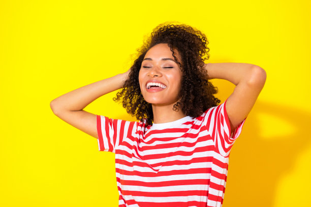 特写照片：年轻迷人的卷发女孩双手托着头，放松休息，终于度假，背景为黄色。图片下载