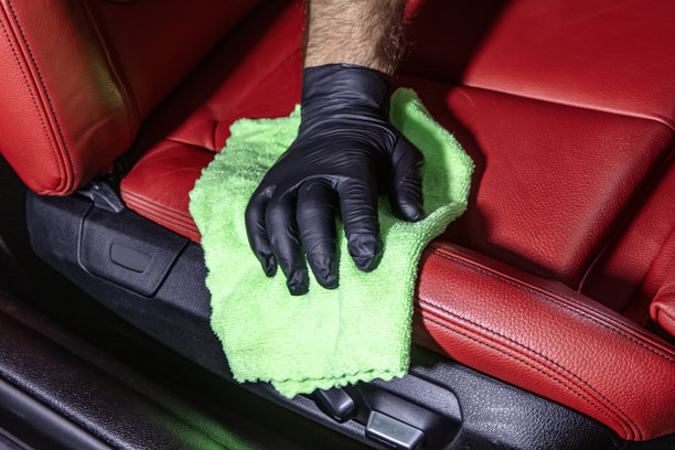 用绿色超细纤维布手工清洁汽车内饰。手持超细纤维布清洁皮革座椅，汽车美容和清洗概念，洗车内饰护理。图片下载
