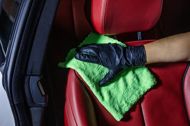用绿色超细纤维布手动清洁汽车内饰。手持超细纤维布清洁皮革座椅，汽车美容和清洗概念，洗车内饰护理。图片下载