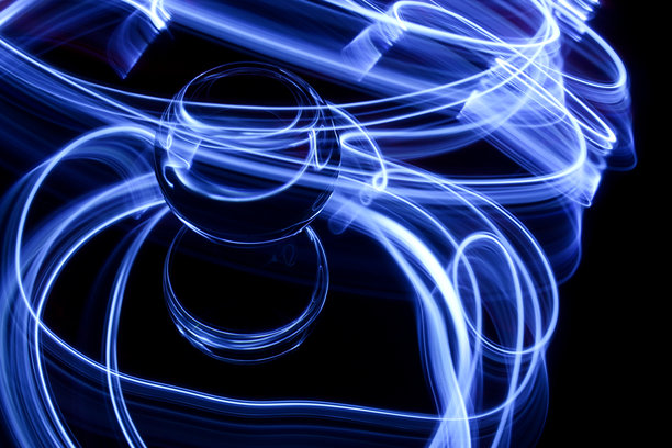 长时间曝光的照片。光绘摄影。在镜子上的玻璃球周围和背后环绕着电蓝色的光旋涡。图片下载