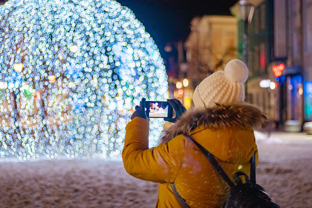 女性游客用智能手机拍摄节日城市装饰的照片。图片下载