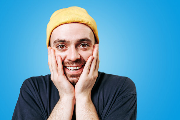 一个戴着黄色帽子的大胡子男人，蓝色背景的摄影棚照片，惊讶的表情图片下载