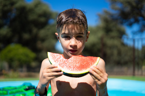 一个阳光明媚的夏天，男孩在泳池里吃西瓜的照片图片下载
