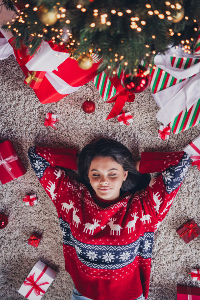 高角度照片，梦幻可爱的女孩穿着新款红色印花衣服，双手举过头顶，躺在地板上享受室内假期。图片下载
