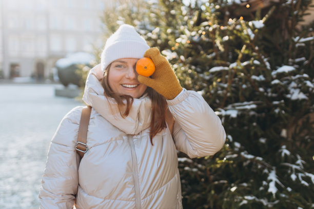 快乐无忧的红发女孩微笑着、笑着，手里拿着橘子靠近眼睛，享受乐趣。冬季假期横幅。假期、节日和幸福的概念，圣诞节。高质量照片图片下载