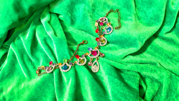女性金色珠宝，镶嵌多彩宝石，背景为明亮的绿色。背景设计，摄影新颖。纺织品，面料模板，现代照片。图片下载
