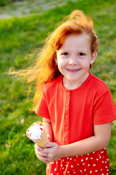 一个小女孩在公园的绿色草坪上吃着夏天的冰淇淋，一张明亮的夏日儿童假期照片，一个小女孩在夏天笑着玩图片下载