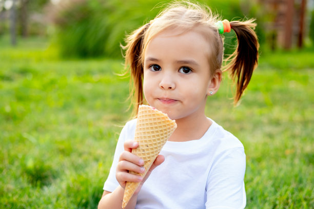 一个小女孩在公园的绿色草坪上吃着夏天的冰淇淋，一张明亮的夏日儿童假期照片，一个小女孩在夏天笑着玩图片下载