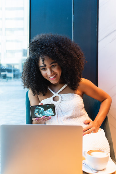 微笑的黑人孕妇向笔记本电脑展示婴儿超声波照片图片下载