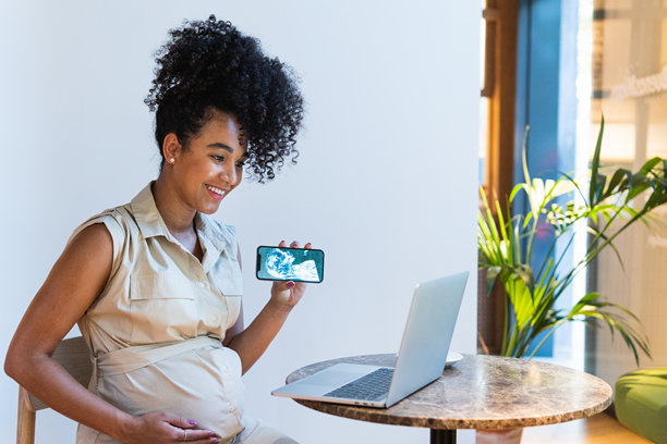 微笑的黑人孕妇向笔记本电脑展示婴儿超声波照片图片下载