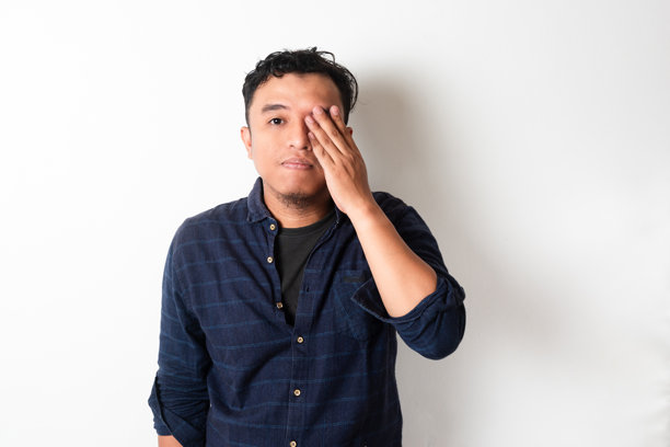亚洲男子用手遮住一只眼睛，表达疲惫或沮丧。他中性而疲惫的表情暗示着压力或沉思，使这张图片非常适合情感和倦怠的主题。图片下载