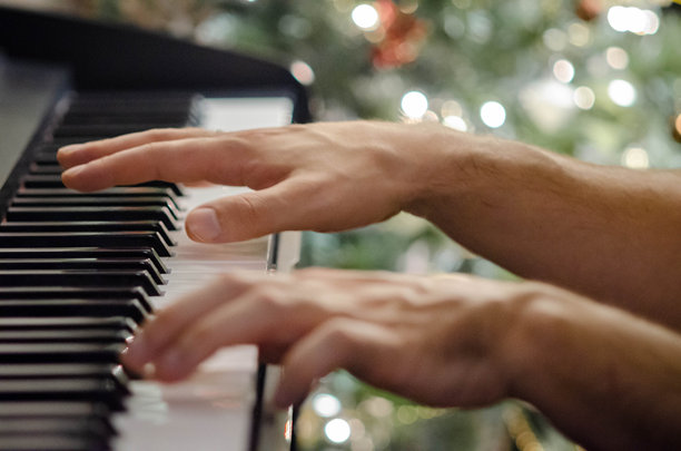 年轻男子在圣诞树旁弹钢琴，特写镜头 - 股票照片图片下载