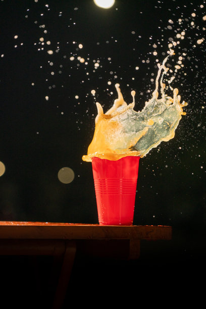 一张高速拍摄的照片，橙色液体从红色塑料杯中溅出，背景为黑色。水花在空中定格，捕捉了十月节庆祝活动的活力与兴奋。图片下载