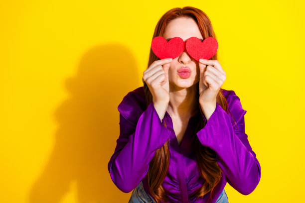 漂亮年轻女孩的照片肖像，手捂眼睛亲吻，穿着时尚的紫色服装，背景为黄色。图片下载