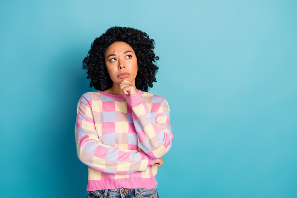 可爱的年轻女士的照片肖像，怀疑的表情，空旷的空间，穿着时尚的粉色格子服装，背景为蓝色。图片下载