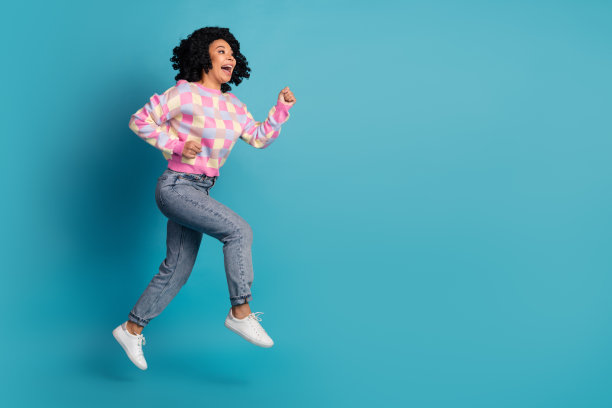 穿着时尚粉色格子服装的可爱年轻女士在蓝色背景下兴奋地奔跑，展现全身照片。图片下载