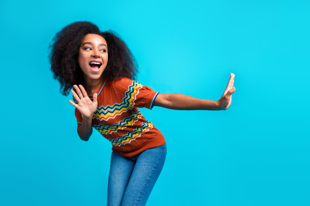 穿着时尚T恤的年轻美国女孩在蓝色背景下放松地跳舞，展现全身长度的照片，适合度假海滩派对。图片下载