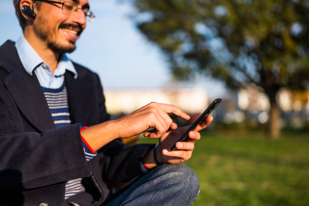 身穿外套、戴着眼镜和入耳式耳机的商人在户外使用手机的特写照片图片下载