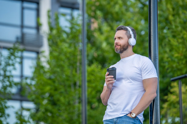 戴着音乐耳机的男子在户外放松。戴着音乐耳机的男子与咖啡的照片。图片下载