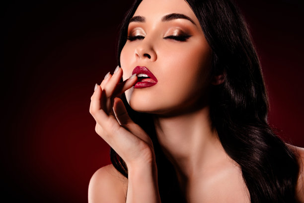 特写剪裁照片，惊艳模特女孩用手指触碰嘴唇，闭着眼睛，背景为深红色。图片下载