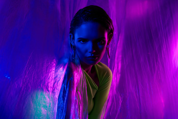 漂亮模特女孩在霓虹灯背景下，穿着绿色裙子，透过透明窗帘摆姿势的照片图片下载