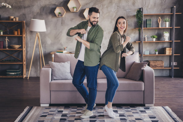 可爱的迷人男女穿着休闲衬衫在室内公寓房间里微笑跳舞的照片图片下载