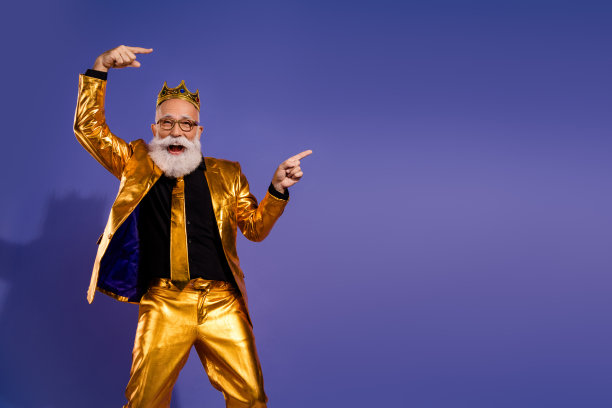 穿着华丽时尚金色服装的老派男子在紫色背景前指向空旷的地方的照片肖像图片下载