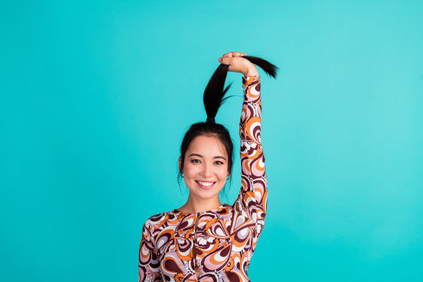 漂亮年轻女孩的照片肖像，扎着马尾辫，穿着时尚多彩的衣服，背景为青色。图片下载