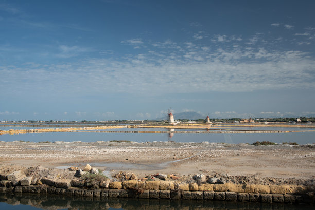西西里岛特拉帕尼的盐田风景照片。盐池清晰可见，映衬着蓝天。背景中有风车。图片下载