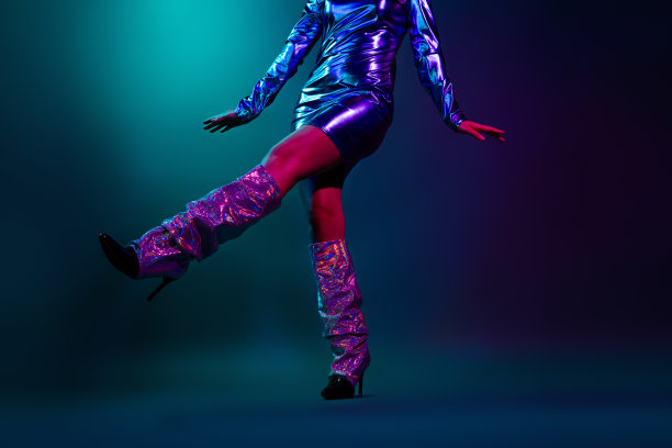 裁剪的照片，漂亮年轻女孩在舞蹈表演中展示腿部，穿着时尚的迪斯科复古服装，背景为深色。图片下载