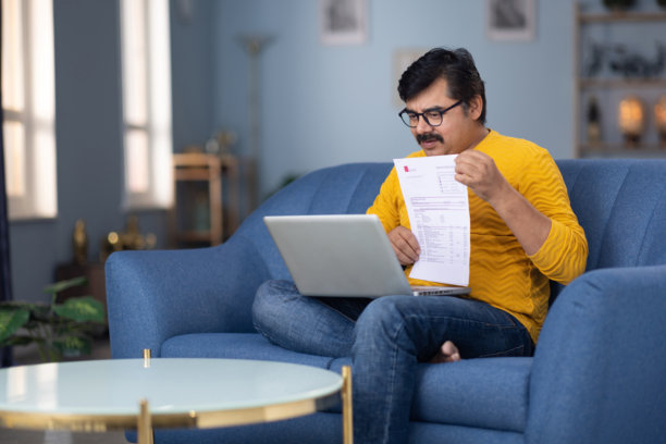 男人坐在家里的沙发上用笔记本电脑阅读文件的库存照片图片下载