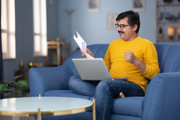 男人坐在家里的沙发上用笔记本电脑阅读文件的库存照片图片下载